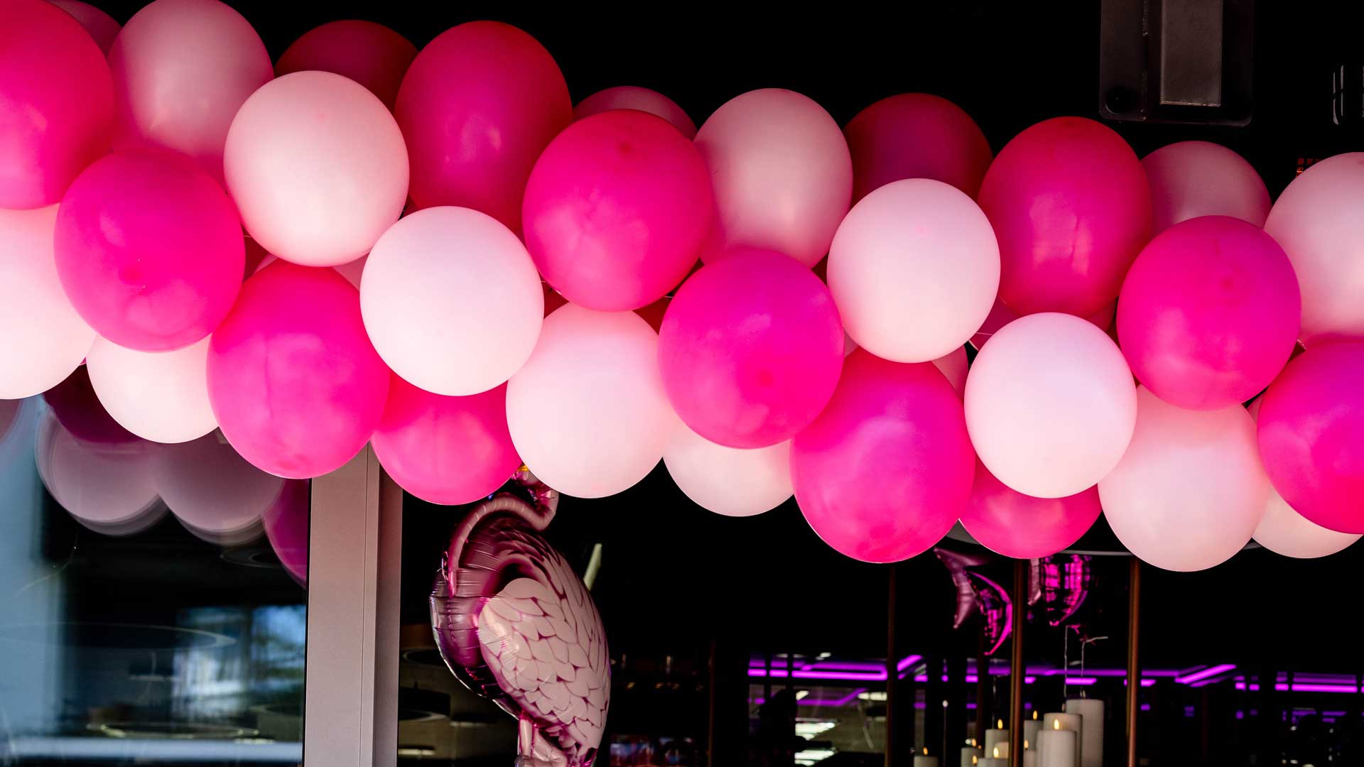 Dekoration aus rosa und pinken Luftballons am Eingang zum Wintergarten und Restaurant. Im Vordergrund sind grÃ¼ne Pflanzen unscharf zu sehen.
