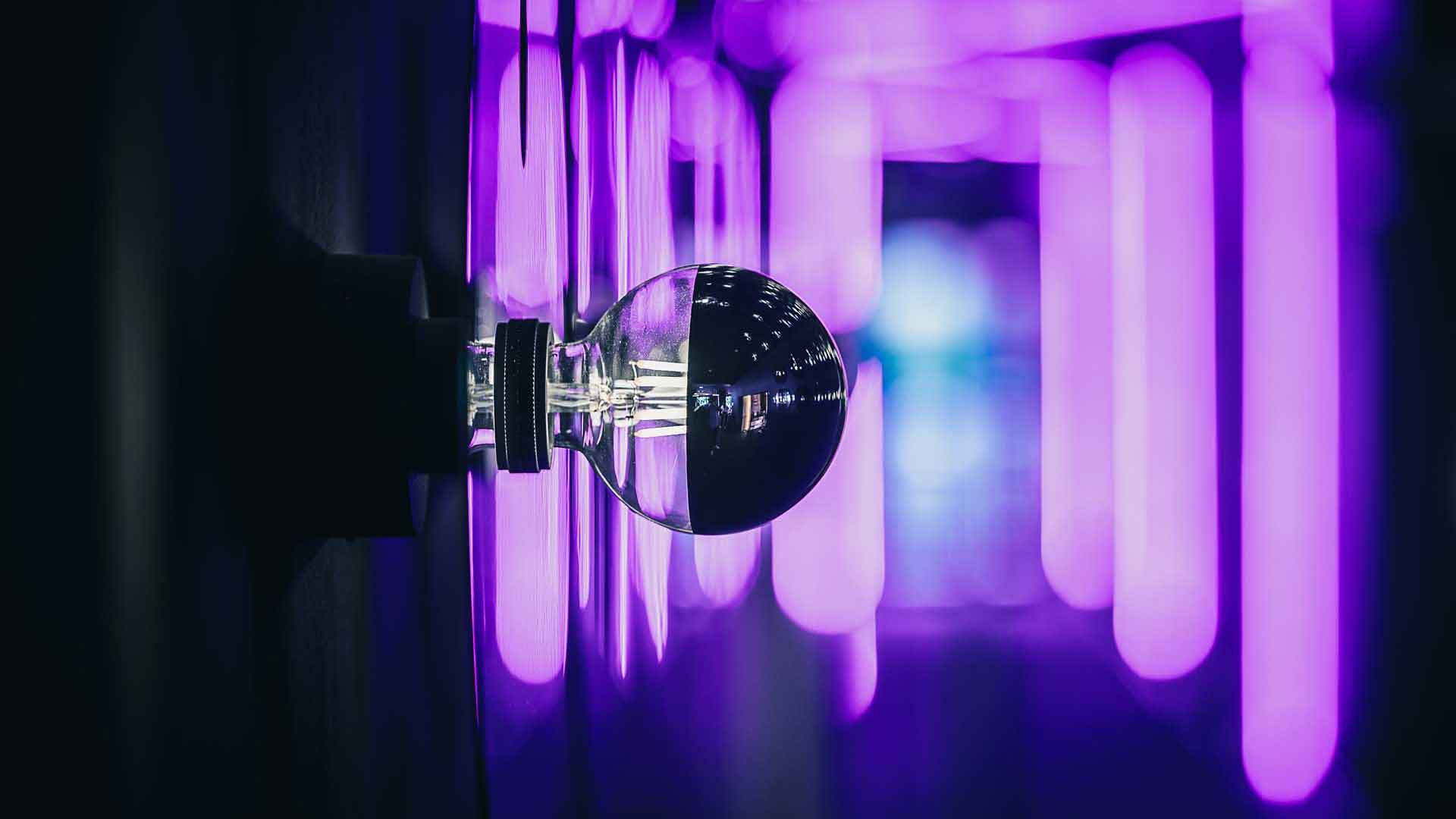 Eine Nahaufnahme einer Glühbirne an einer Wand im Eingang zum Six Zero, die von lila Neonlichtern umgeben ist. Die Lichter reflektieren sich auf der Oberfläche der Glühbirne und schaffen eine futuristische, stimmungsvolle Atmosphäre.